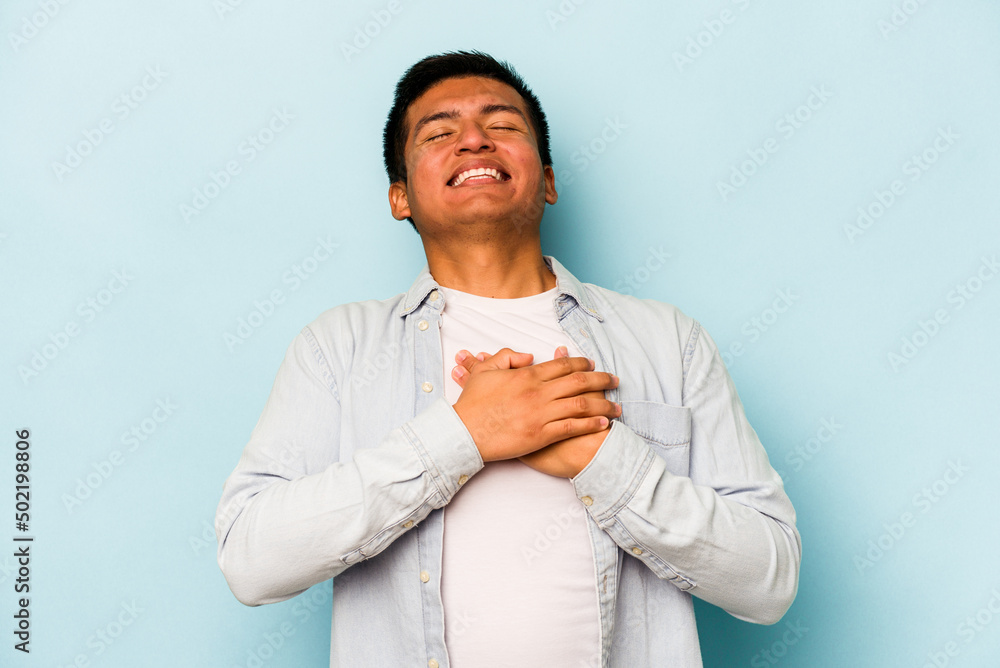 Young hispanic man isolated on blue background laughing keeping hands on heart, concept of happiness. Young hispanic man isolated on blue background laughing keeping hands on heart, concept of happiness.