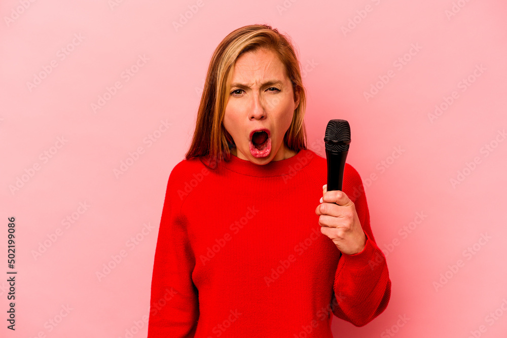 Young caucasian singer woman isolated on pink background screaming very angry and aggressive. Young caucasian singer woman isolated on pink background screaming very angry and aggressive.