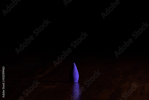 Violet incense cone on a wooden surface with a dark background.