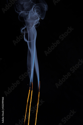 Close-up image of three golden-colored incense sticks burning and blue smoke rising to the top. Copy Space. photo