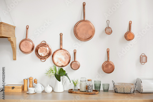 Different kind of cookware and ceramic plates on tabletop wooden kitchen. Set of copper saucepans, pans, pots and ladle hanging in kitchen. Hanging kitchen utensil on wall. kitchen interior decor	 photo