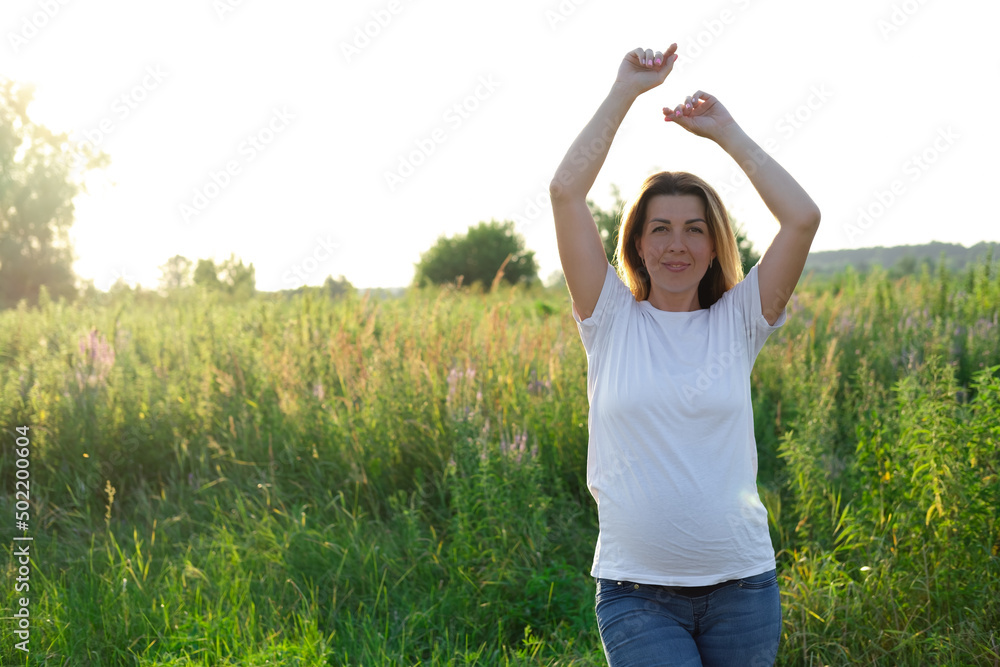 cute pregnancy portrait. happy mother to be with a big belly in white t-shirt and jeans outside on the meadow at sunset