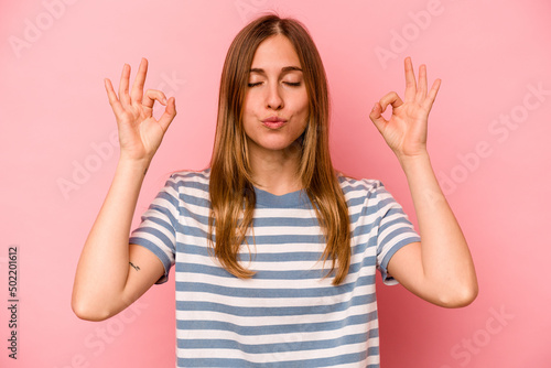 Young caucasian woman isolated on pink background relaxes after hard working day, she is performing yoga.