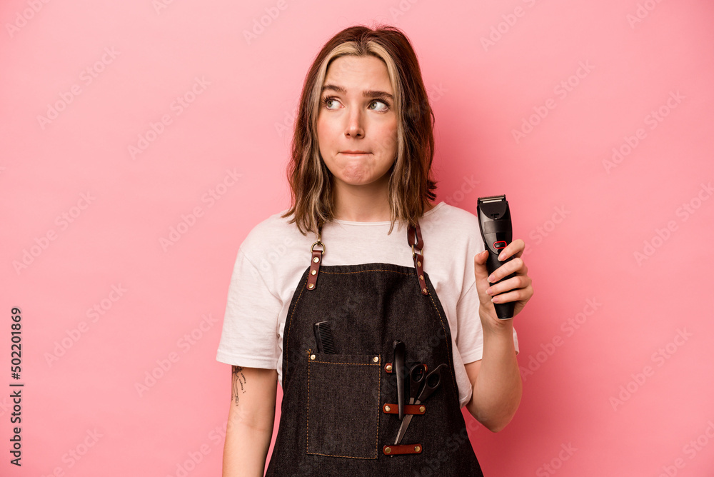 Young hairdresser woman holding scissors isolated on pink background confused, feels doubtful and unsure. Young hairdresser woman holding scissors isolated on pink background confused, feels doubtful and unsure.