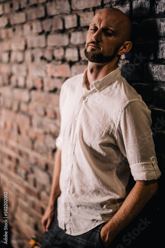 Portrait of a bald man with a beautiful beard in a white shirt on a brick background