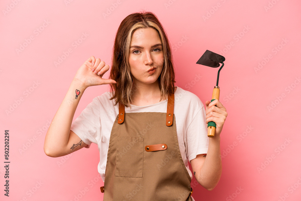 Young gardener woman holding gardening shovel isolated on pink background feels proud and self confident, example to follow. Young gardener woman holding gardening shovel isolated on pink background feels proud and self confident, example to follow.
