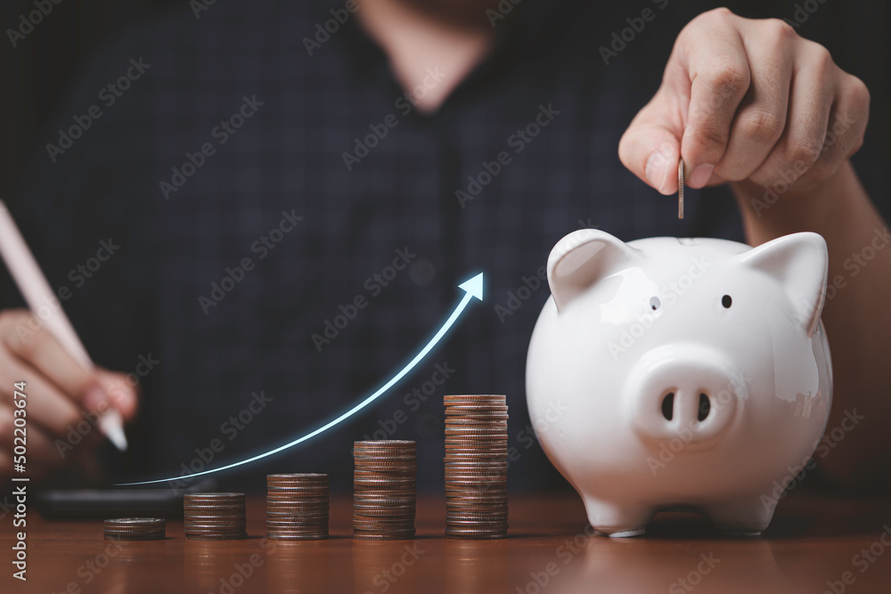 Businessman putting coin to white piggy bank with coins stacking and increasing arrow for growth deposit saving money and increase dividend profit investment concept. - obrazy, fototapety, plakaty 