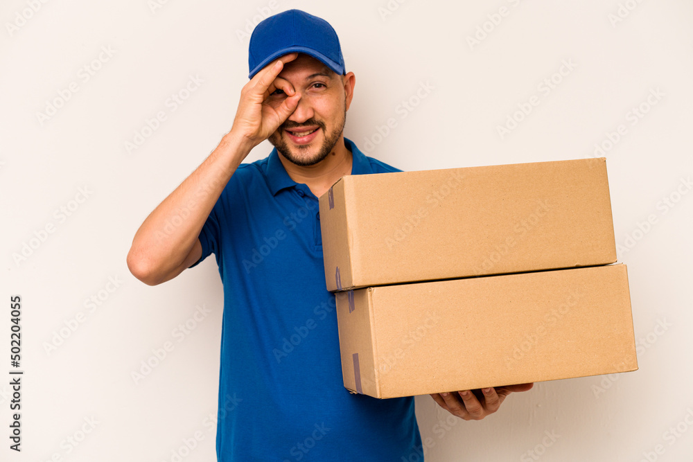Hispanic delivery man isolated on white background excited keeping ok gesture on eye. Hispanic delivery man isolated on white background excited keeping ok gesture on eye.