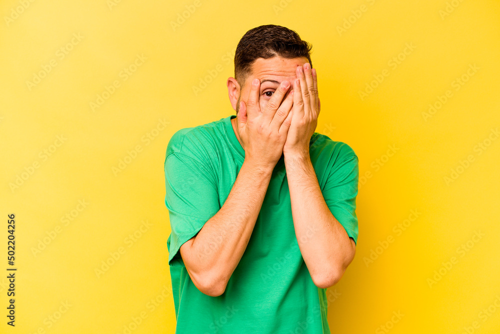 Young hispanic man isolated on yellow background blink through fingers frightened and nervous. Young hispanic man isolated on yellow background blink through fingers frightened and nervous.