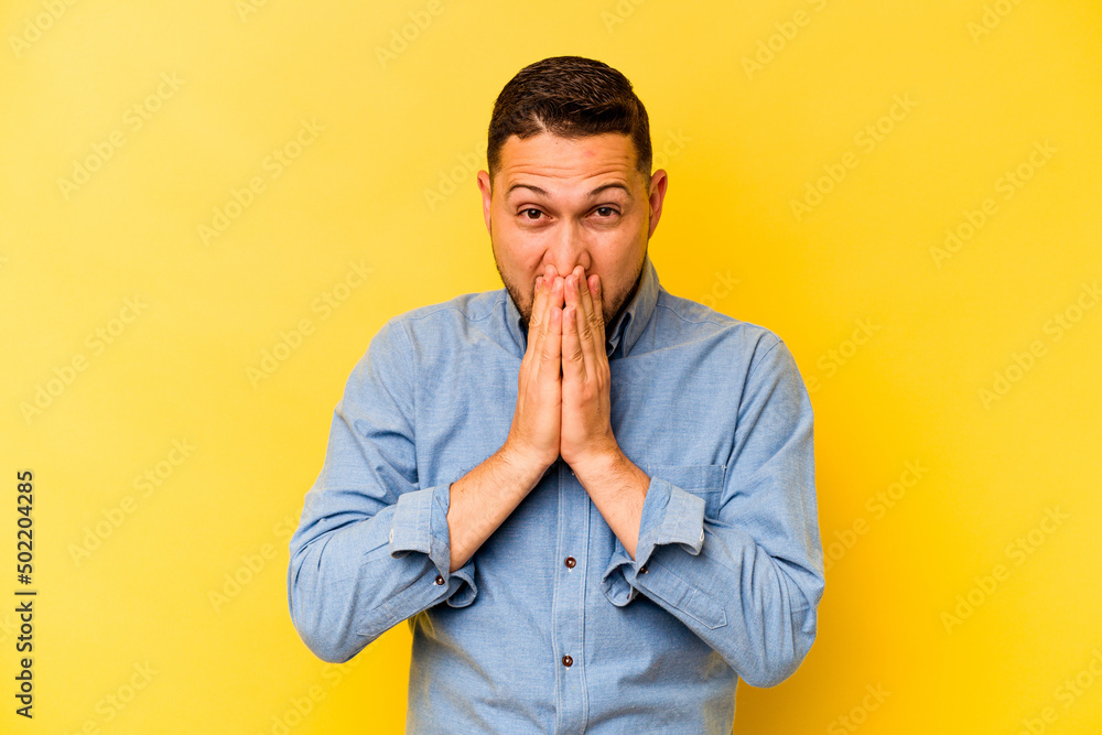 Young hispanic man isolated on yellow background shocked covering mouth with hands. Young hispanic man isolated on yellow background shocked covering mouth with hands.