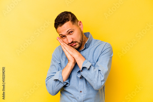 Young hispanic man isolated on yellow background yawning showing a tired gesture covering mouth with hand. © Asier