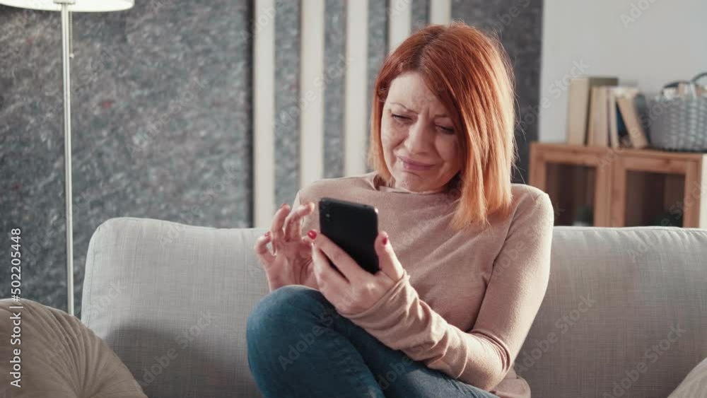 Adult woman sit on couch hold cellphone read unpleasant news bad sms feels upset start crying. Adult woman sit on couch hold cellphone read unpleasant news bad sms feels upset start crying.