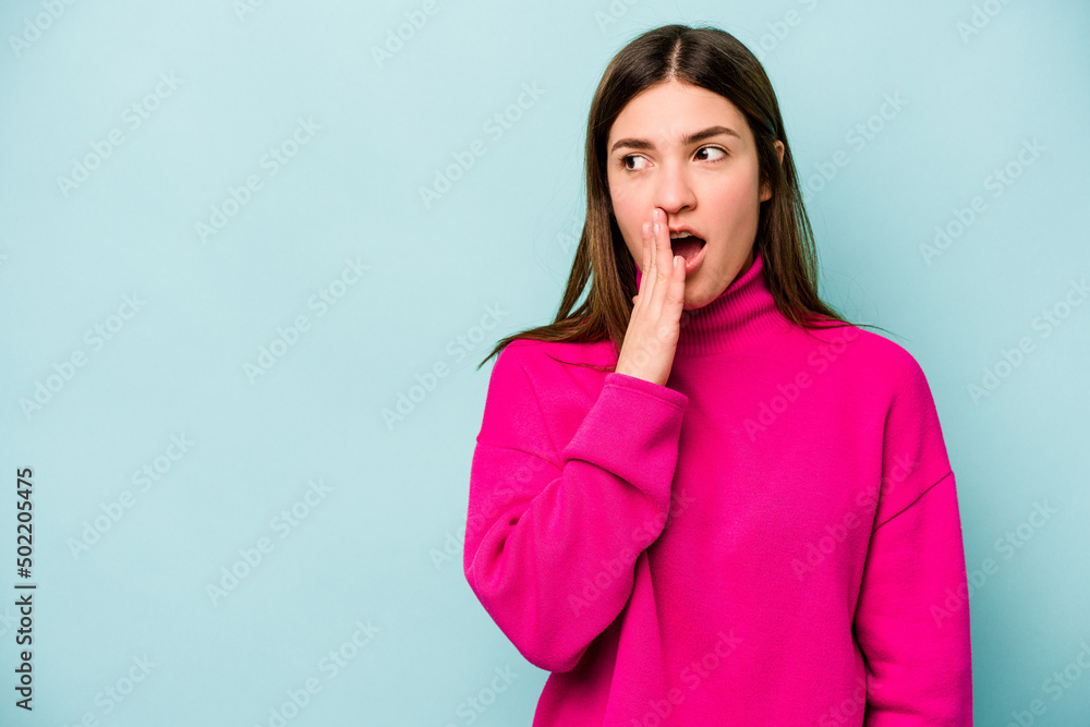 Young caucasian woman isolated on blue background is saying a secret hot braking news and looking aside Young caucasian woman isolated on blue background is saying a secret hot braking news and looking aside