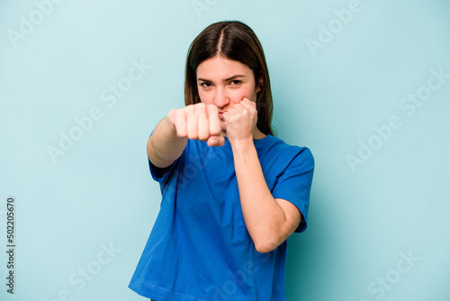 Young caucasian woman isolated on blue background throwing a punch, anger, fighting due to an argument, boxing.