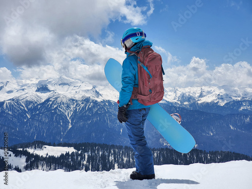 Young active woman with snowboard standing at snowy mountains background photo