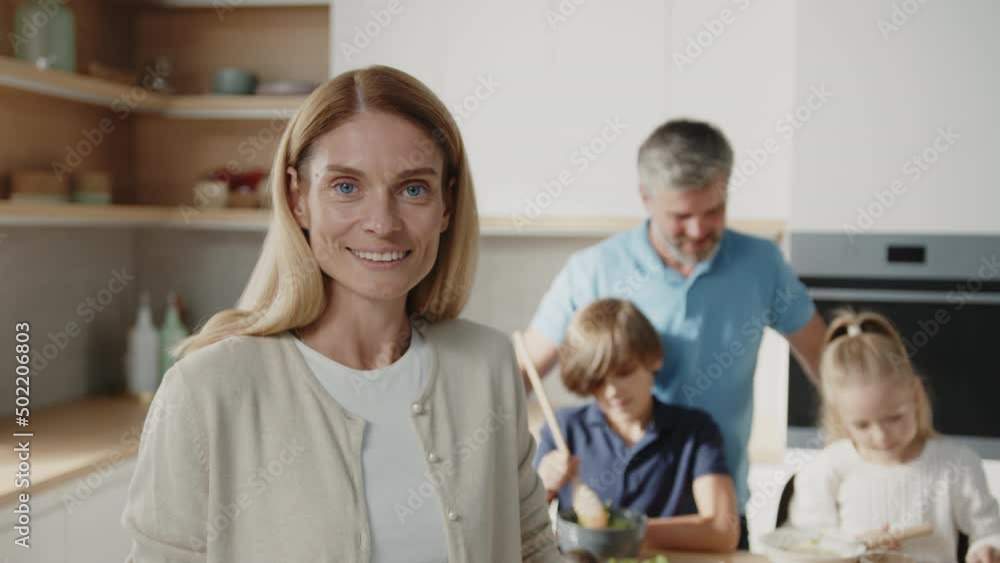 Beautiful caucasian woman standing in the kitchen and smiling to the camera. Beautiful family with little kids prepare breakfast together at home. Beautiful caucasian woman standing in the kitchen and smiling to the camera. Beautiful family with little kids prepare breakfast together at home.