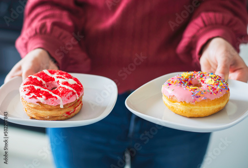 A woman holding and serving two tasty pink donuts on a plate photo