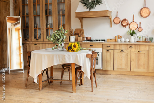 Stylish dining room with furniture in retro style. Cozy Wooden cuisine decorated with summer decor. Kitchen utensils, dishes, plates. Interior design scandinavian kitchen with round table and chairs