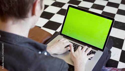 Close-up of young man typing at laptop with green scree. Stock footage. Young programmer or freelancer working at laptop with green screen