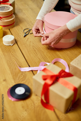 Hands of unrecognisable woman wrapping with ribbon a pink present, gift box, christmas or other holiday handmade present, Making bow at present box, decoration of gift