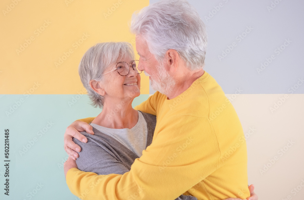 Beautiful attractive Caucasian elderly couple hugging each other on isolated colored background. White-haired seniors look into each other's eyes, smiling, enjoying good company and retirement Beautiful attractive Caucasian elderly couple hugging each other on isolated colored background. White-haired seniors look into each other's eyes, smiling, enjoying good company and retirement
