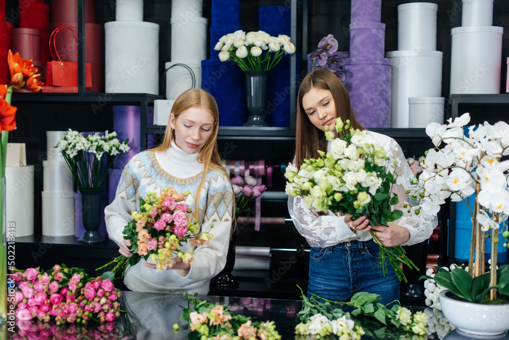 Fototapeta premium Two young women take orders by phone and make beautiful festive bouquets in a cozy flower shop. Floristry and bouquet making in a flower shop. Small business.