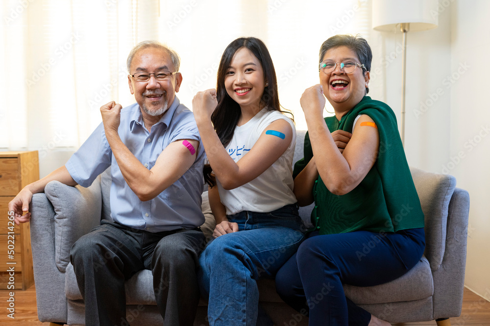 Senior Asian couple and young woman get vaccinated with bandage on arm show thumb up sign in living room. Grandfather and grandmother get vaccine.