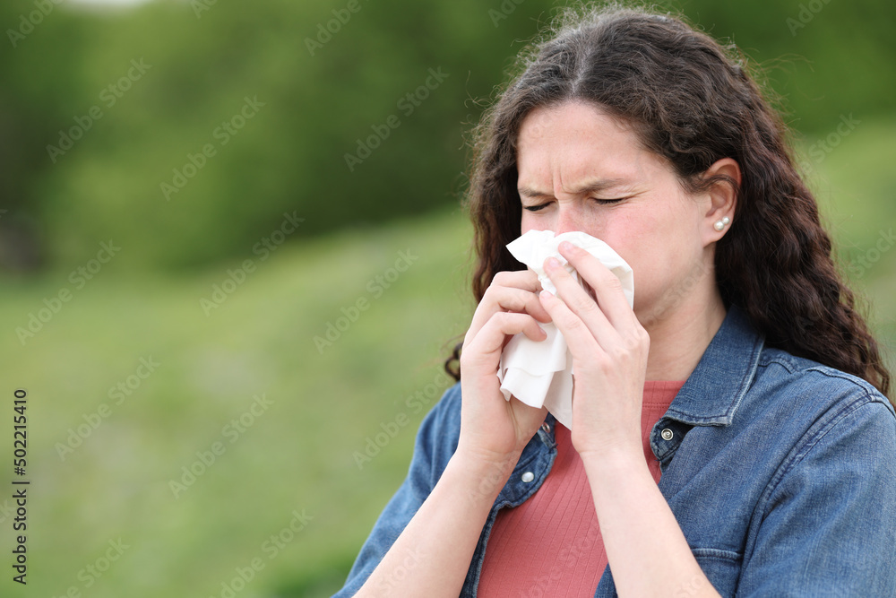 Ill woman blowing on tissue in a park Ill woman blowing on tissue in a park