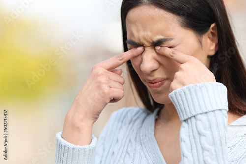 Woman scratching itchy eyes with her hands in a park