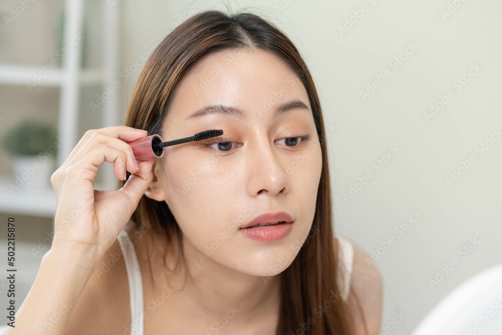Happy beauty concept, cute asian young woman, girl smile, make up face hand by applying mascara brush on eyelash, looking into mirror in morning routine at home. People look with natural fashion style Happy beauty concept, cute asian young woman, girl smile, make up face hand by applying mascara brush on eyelash, looking into mirror in morning routine at home. People look with natural fashion style
