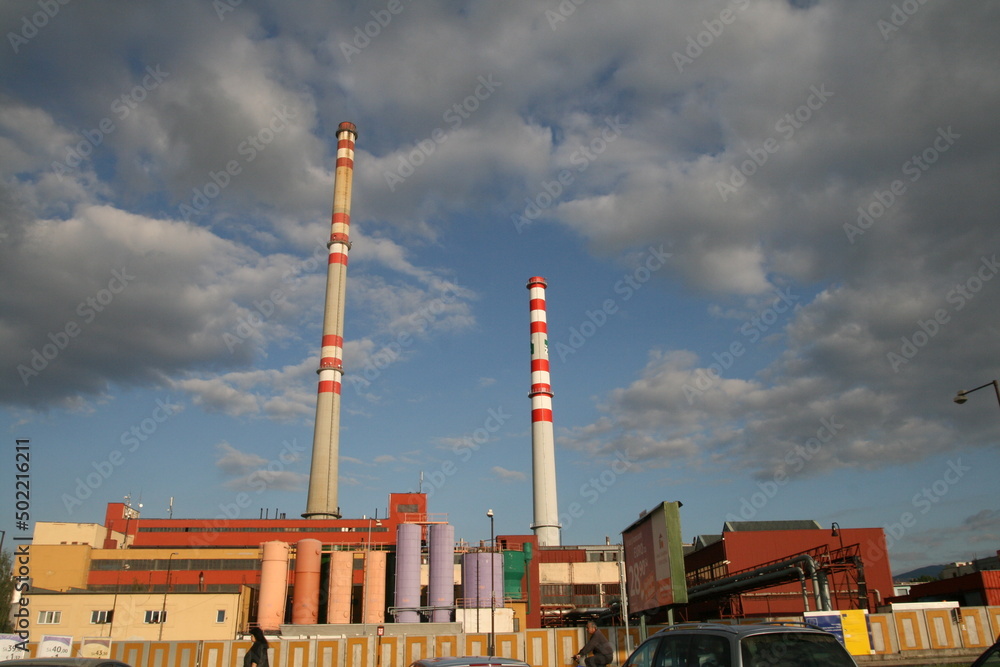 Plant tanks painted in different colors. Two factory chimneys rest against the summer sky with clouds