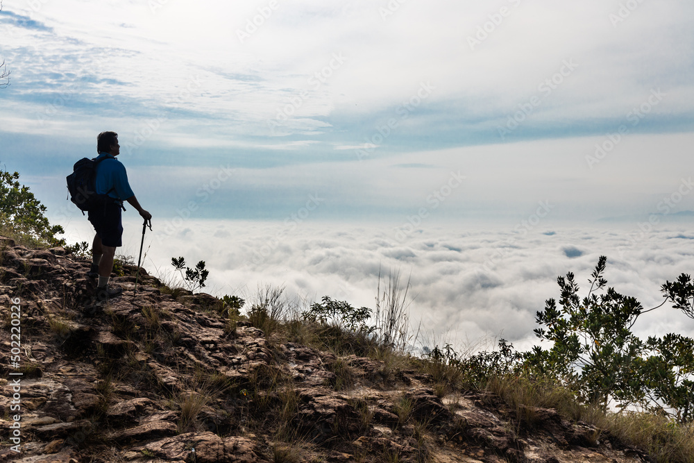 Hiker Asian man in silhouette standing on peak of mountain admiring cloud scape and sunrise
