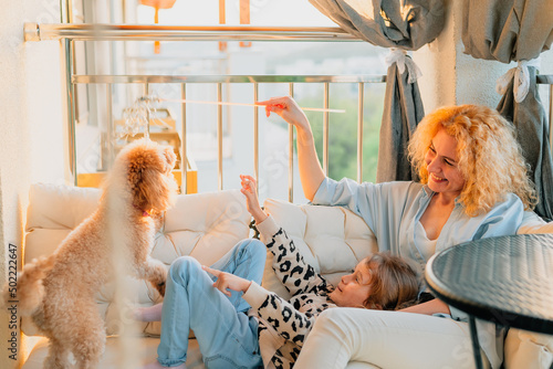 a little, happy girl, a child with a smile plays on a summer, spring vernada at home with mom and a dog at sunset. family weekend evening. dog, pets as a family member.