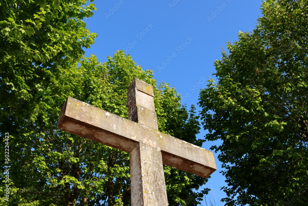 A large marble cross against the backdrop of green trees and a blue sky. Granite Cross.
