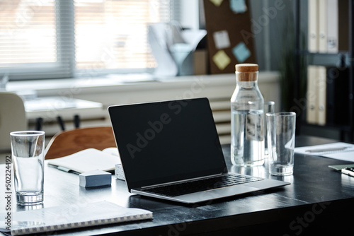 Close up of opened laptop and water bottle on meeting table in office, copy space