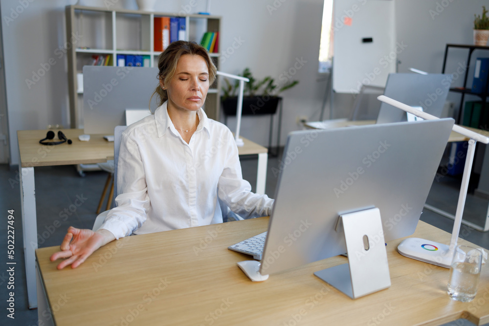 Calm businesswoman meditating at office desk with eyes closed Calm businesswoman meditating at office desk with eyes closed