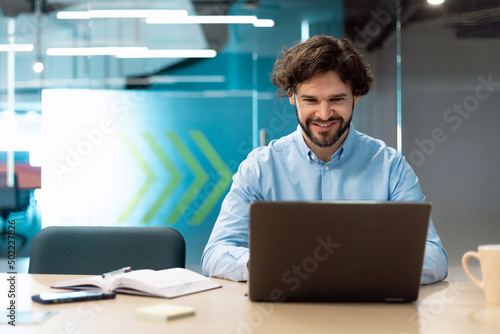 Smiling businessman using laptop sitting at desk in office photo