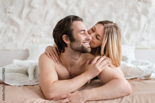 Foto Affectionate young couple lying together in bed, hugging and kissing after lovemaking
