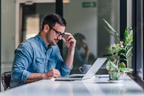 Bilde på lerret Confident professional wearing eyeglasses using laptop at table in home office