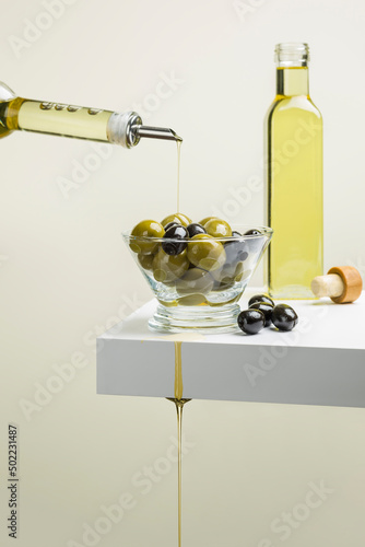 Big green and black olives in glass bowl on shelf with oil bottle