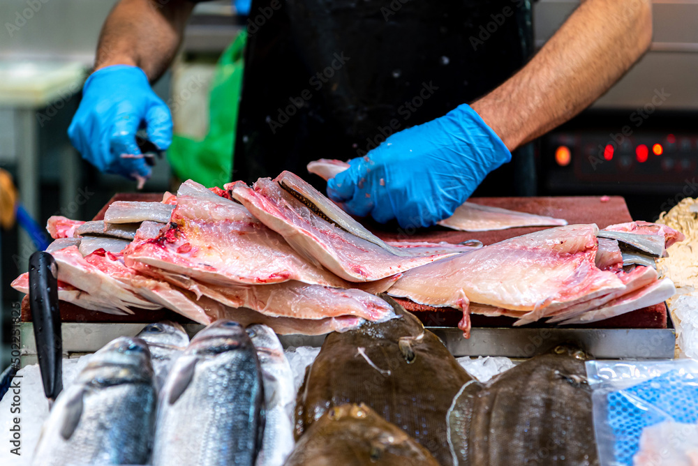 A stall at the fish market. Men's hands in blue rubber gloves butcher sea fish