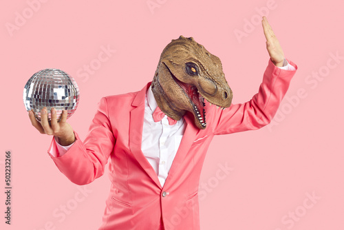 Fotobehang Cheerful, stylish and fashionable man in dinosaur rubber mask with disco ball in his hand on pastel pink background