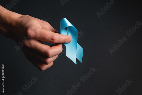 Close up of male hand holding blue ribbon on dark grey background wall. Prostate Cancer Awareness, Movember Men's health awareness. Healthcare, International men, Father and World cancer day concept photo