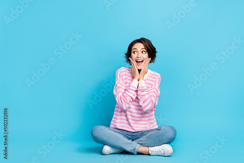 Portrait of impressed astonished girl sitting floor see huge bargain on black friday isolated on blue color background