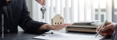 Sales manager or real estate agent holds the key handing it to the customer after signing the house purchase contract with home insurance, Trading of mortgages and insurance concept.