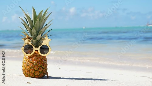 Pineapple in funny sunglasses on caribbean sandy beach. Tropical vacation photo