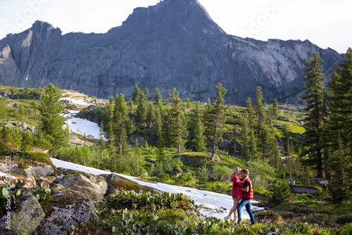Beautiful young woman and man walk, hug and kiss in mountain nature at sunse
