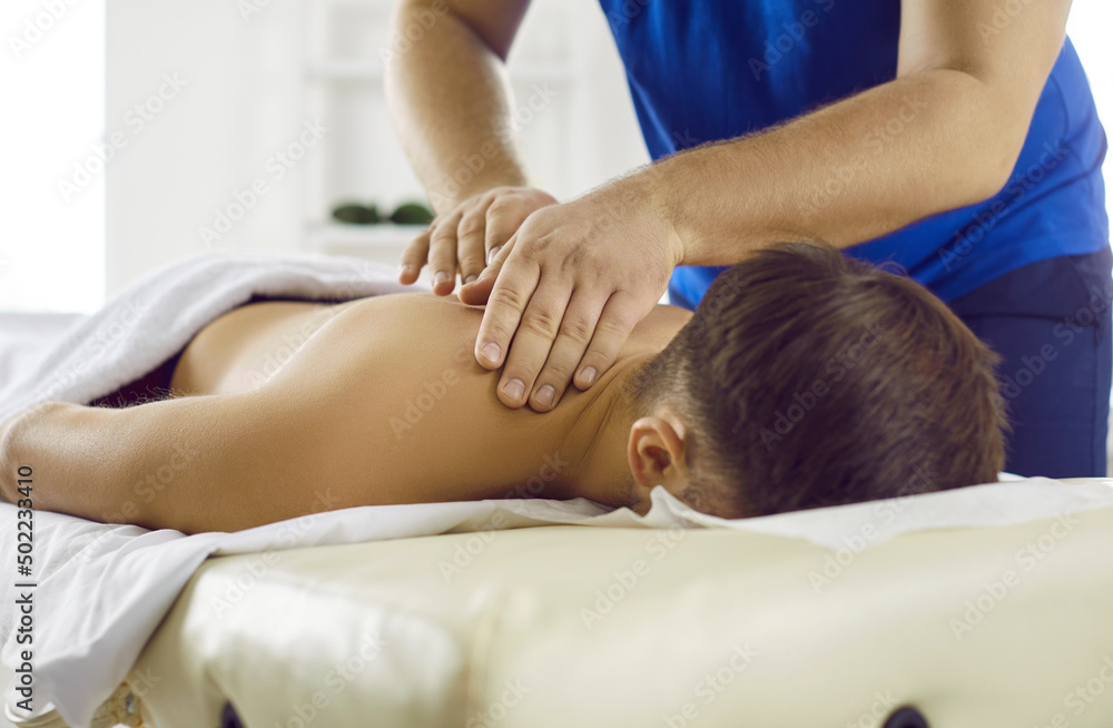 Man getting treatment in health spa. Masseur in modern health center performs therapeutic body massage for young man. Concept of rest, pleasure, health and alternative medicine. Cropped image. Man getting treatment in health spa. Masseur in modern health center performs therapeutic body massage for young man. Concept of rest, pleasure, health and alternative medicine. Cropped image.