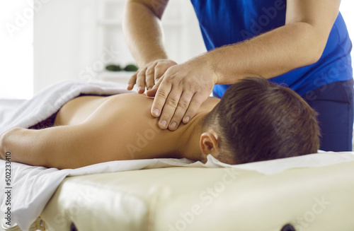 Man getting treatment in health spa. Masseur in modern health center performs therapeutic body massage for young man. Concept of rest, pleasure, health and alternative medicine. Cropped image.