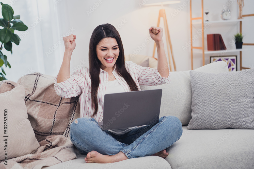 Portrait of attractive cheerful long-haired woman sitting on divan using laptop rejoicing having fun at home indoors Portrait of attractive cheerful long-haired woman sitting on divan using laptop rejoicing having fun at home indoors